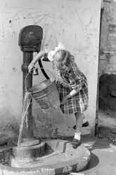 Kleines Mädchen leert einen Eimer Wasser in einen Pumpbrunnen, 9. Mai 1939