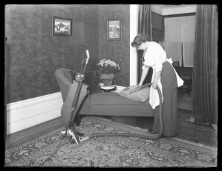 Unidentifizierte Frau demonstriert die Verwendung des Polsteraufsatzes des Apex-Staubsaugers, ca. 1913-14